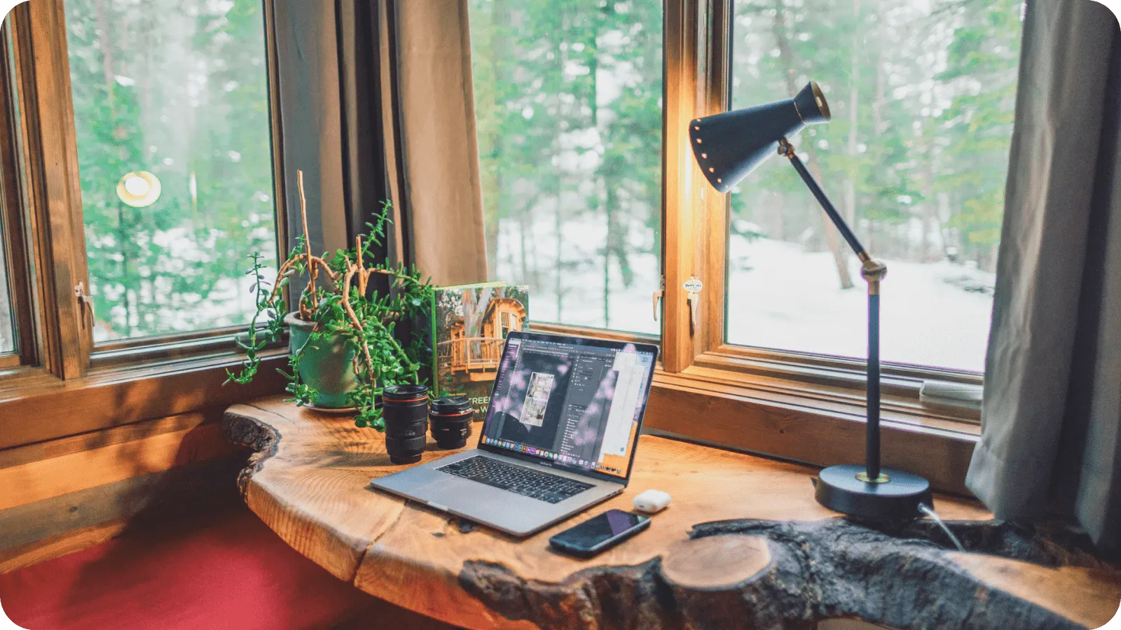 A quiet workspace by a large window with a wooden desk and a lamp