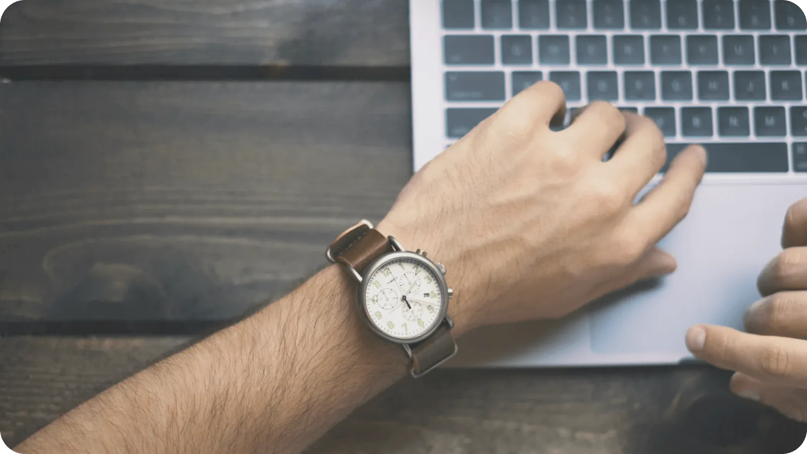 A hand wearing a watch typing on a laptop keyboard